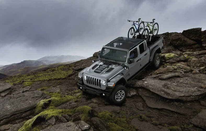 Jeep Gladiator visto de cima em terreno rochoso com duas bicicletas no suporte da caçamba. Ao fundo, o céu está nublado.