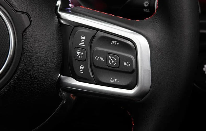 Detalhe dos botões no lado direito do volante do Jeep Gladiator, com opções para ativar o piloto automático adaptativo, com ícones representando o controle de velocidade (botão ao centro), e manter maior (botão superior) ou menor distância (botão inferior).