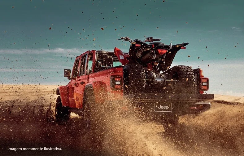 Picape Jeep Gladiator vermelha vista de trás, com quadriciclo na caçamba aberta em terreno arenoso