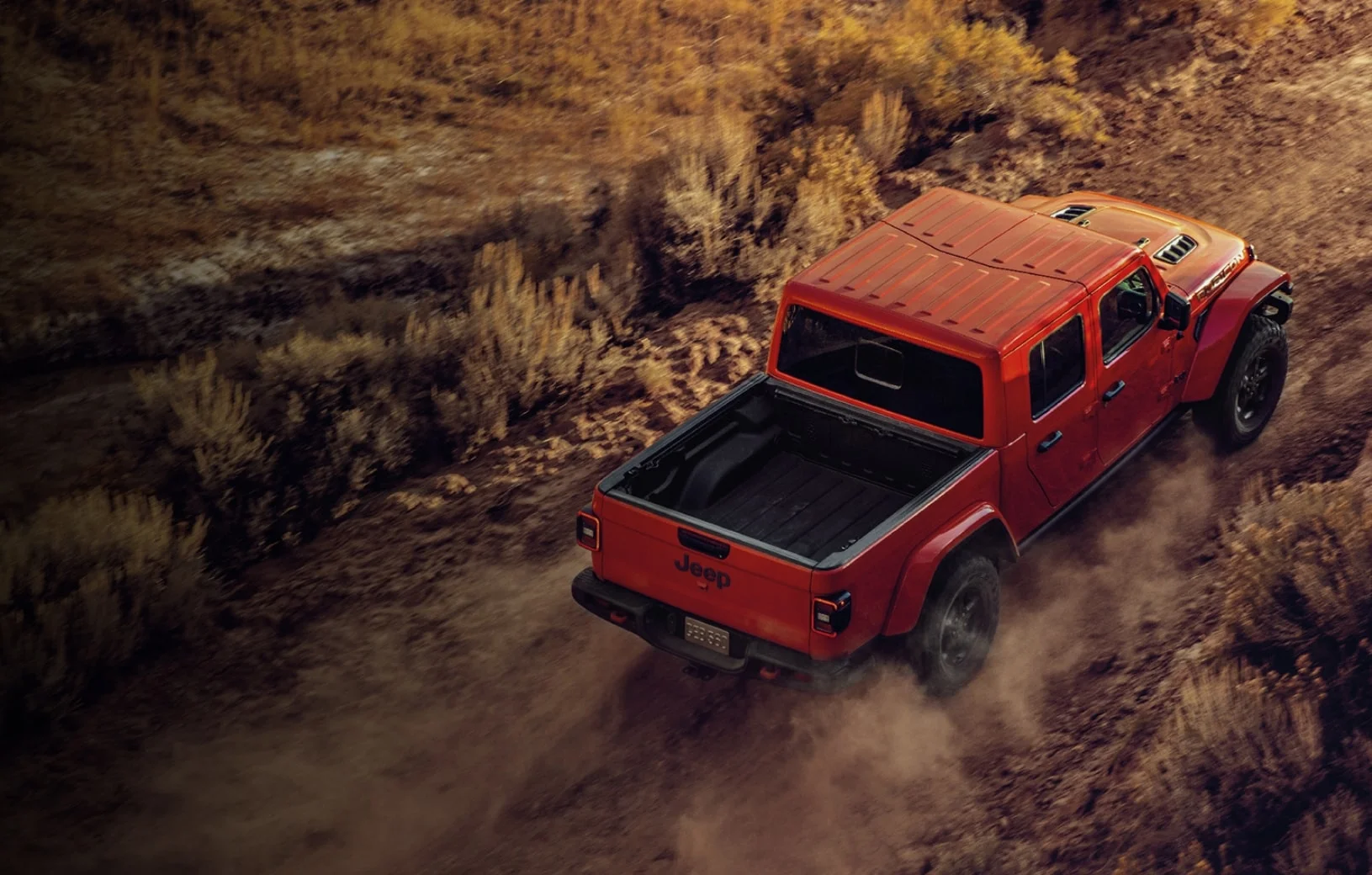 Picape Jeep Gladiator vermelha vista de cima em terreno arenoso.