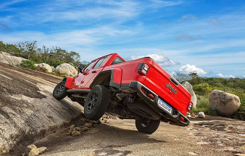 Vista traseira do Jeep Gladiator vermelho inclinado subindo em uma rocha, com pneu traseiro esquerdo sem contato com o solo.